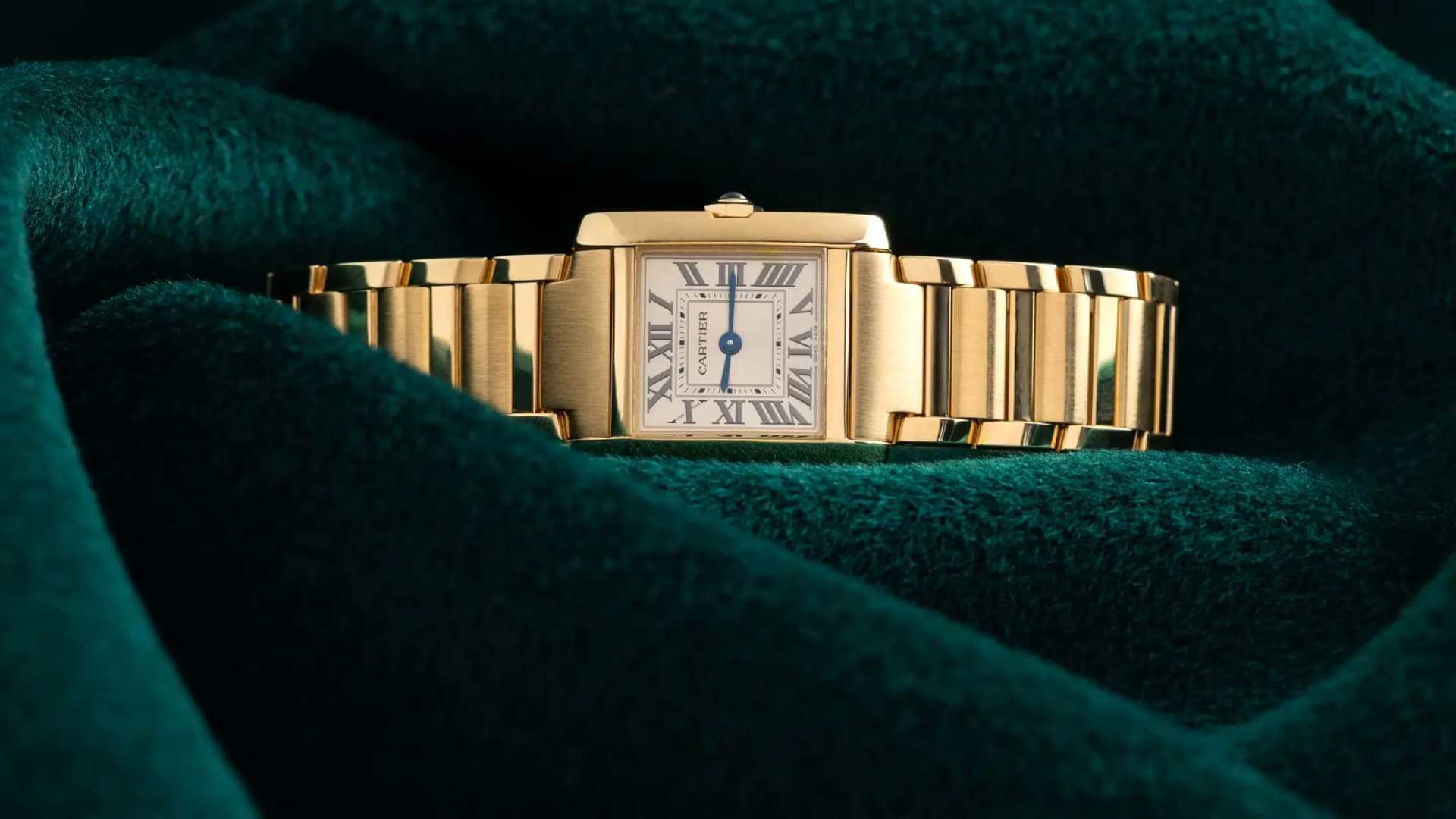 Cartier Tank gold wristwatch with Roman numerals on white dial, displayed on green velvet.