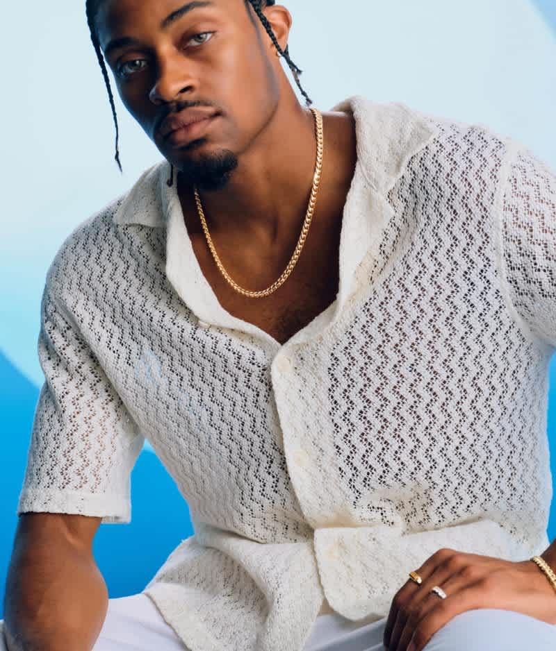 A man models a gold chain worn solo with a light-colored knit shirt, demonstrating a casual styling option