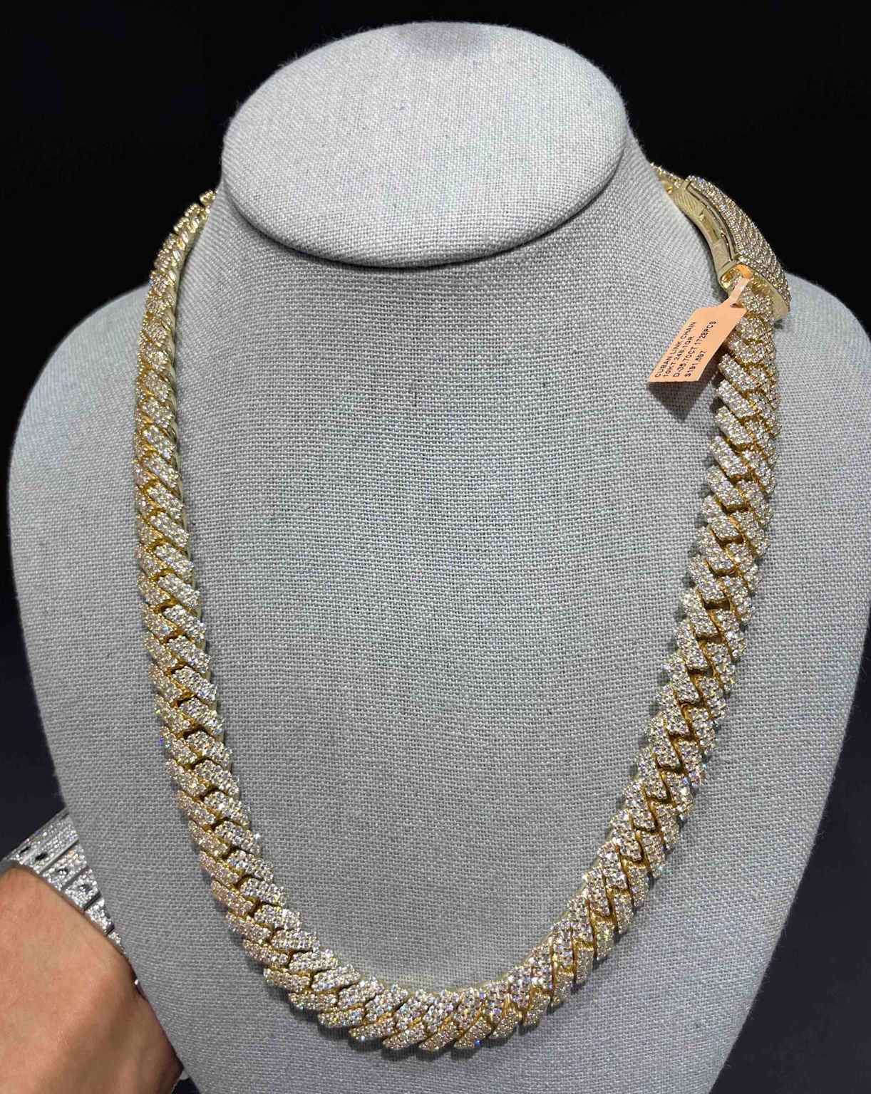 An iced-out Cuban link chain displayed on a jewelry bust, showcasing its diamond-encrusted design
