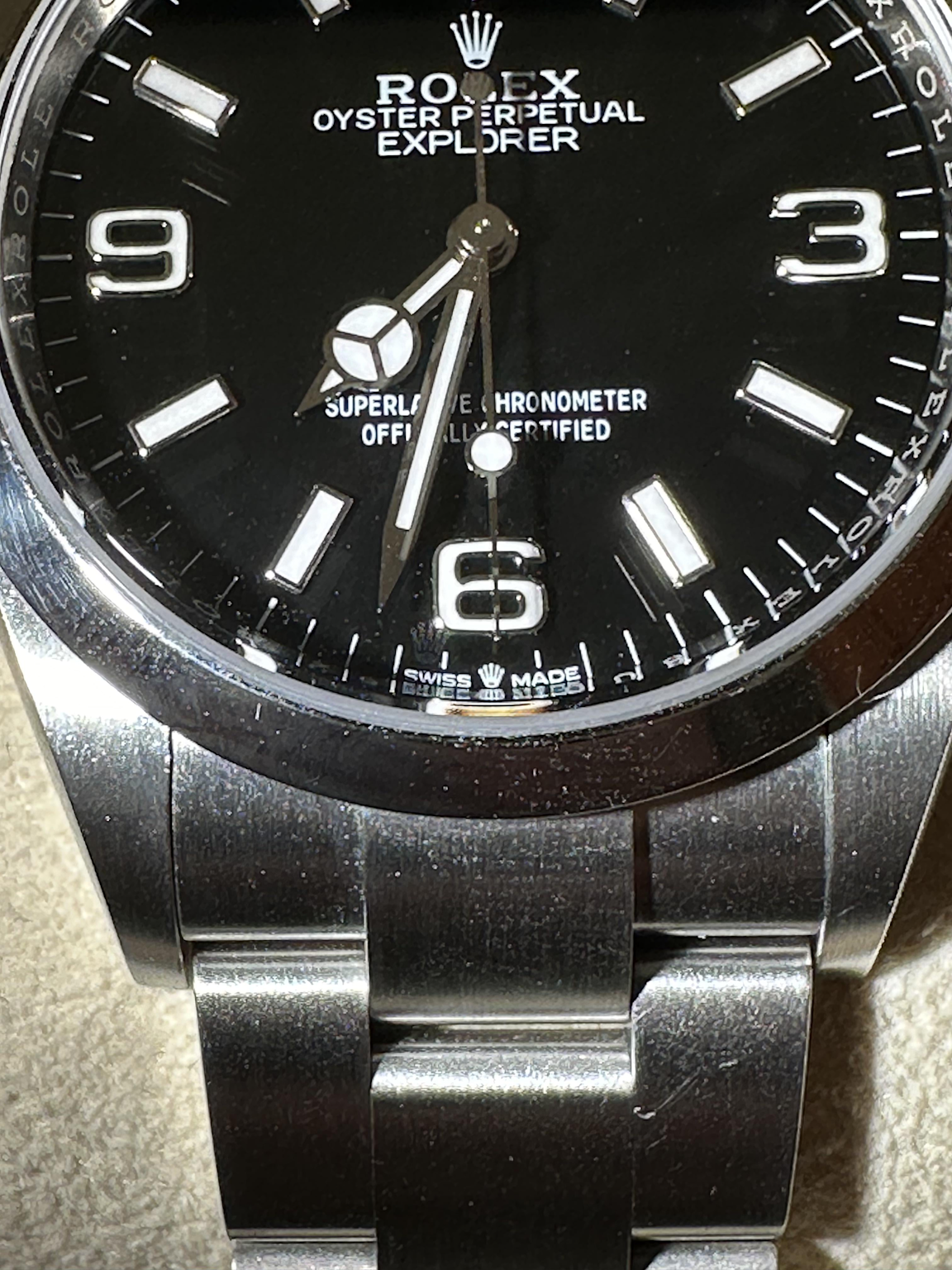 Close-up of Rolex Explorer dial showing laser-etched crown at 6 o'clock on sapphire crystal, a key authenticity feature
