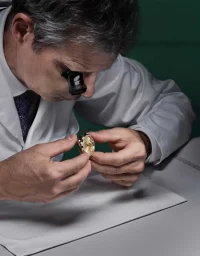 Watchmaker inspecting a luxury gold timepiece under magnification for precision craftsmanship.