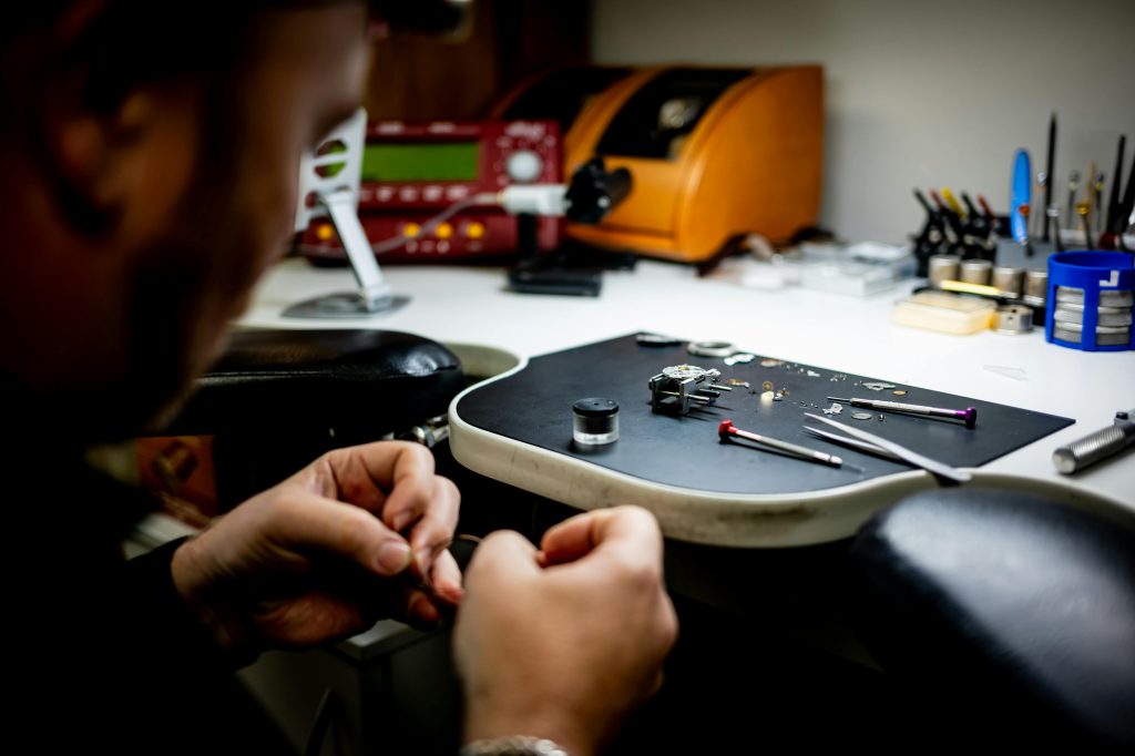 Watchmaker working on luxury timepiece at a professional bench with tools and parts.