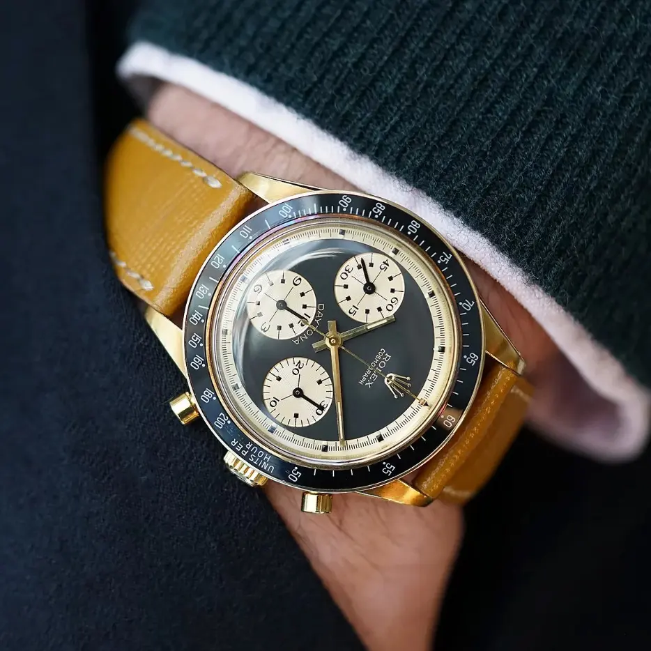 Vintage Rolex Daytona with black Paul Newman dial, gold case, and tan leather strap.