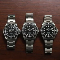 Three Rolex Submariner stainless steel watches with black dials on a wooden surface.