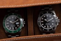 Rolex Submariner Date with green bezel and classic black Submariner side by side in a luxury watch case.