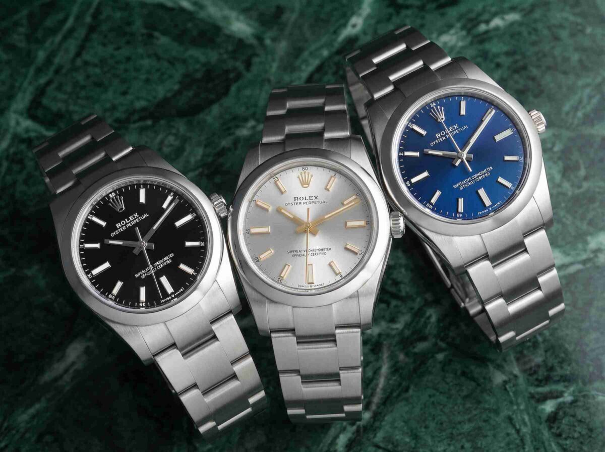 Three Rolex Oyster Perpetual stainless steel watches with black, silver, and blue dials displayed on a green surface.