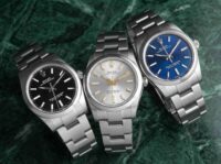 Three Rolex Oyster Perpetual stainless steel watches with black, silver, and blue dials displayed on a green surface.