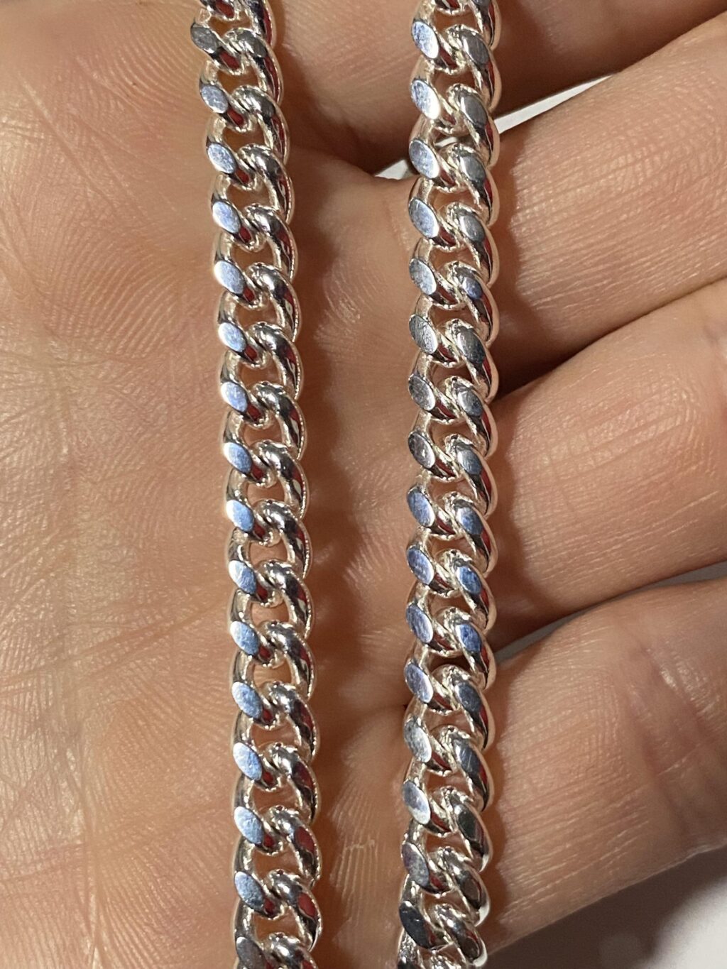 Close-up of two silver Cuban link chains held in a hand, showing polished links and detailed craftsmanship.