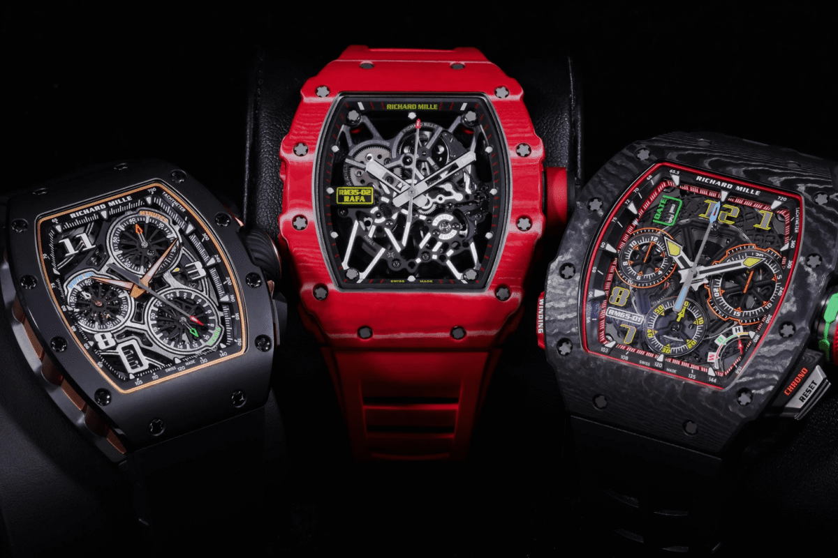 Three Richard Mille skeleton watches in black, red, and forged carbon cases displayed together in a luxury showcase.