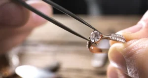 Rose gold diamond engagement ring with solitaire center stone and pavé band held by jeweler tweezers